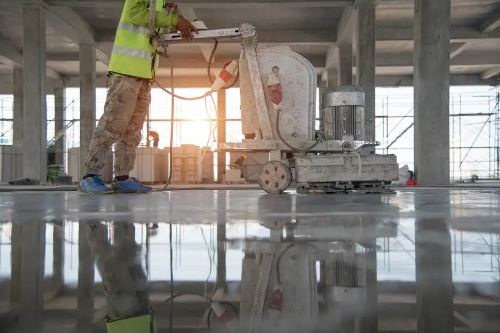 Concrete floor grinder being run across a slab inside an unfinished commercial interior