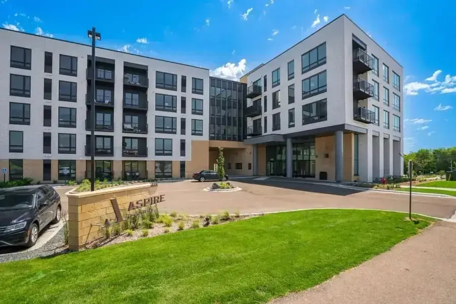 Apartment complex exterior with landscaped grounds and a resident parking area. A neighboring property's own monument sign is visible in the background and is not affiliated with Clean Construction and Building Services.